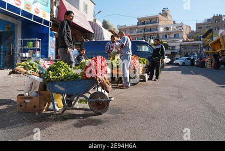 Aqaba, Giordania - 17 gennaio 2020: Uomo arabo sconosciuto in piedi accanto a un grande mucchio di verdure rafano fresco esposto sulla strada in carriola - frutta An Foto Stock
