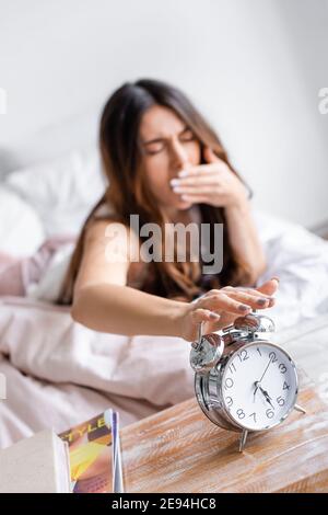 Sveglia sul comodino e vista offuscata della giovane donna che non vuole  svegliarsi, coprendo le orecchie con cuscino nel letto Foto stock - Alamy