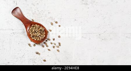 Canapa sbucciata - Cannabis sativa - in piccolo cucchiaio di legno scuro su scrivania in pietra bianca, spazio per il testo sul lato destro Foto Stock