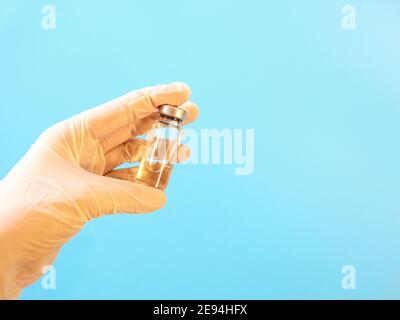 Flacone con vaccino in mano in guanti medici su blu sfondo Foto Stock