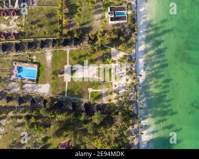 Foto aerea di un hotel di lusso su una spiaggia prima La linea con gli alberi di palma cade le loro tonalità su un alto Marea acqua dell'Oceano Indiano alla sera in Paje Foto Stock