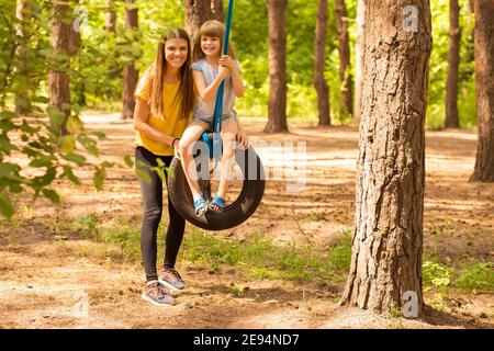 Felice mamma e figlia oscillano sulla ruota con sfondo estate natura. Tempo di famiglia attivo insieme Foto Stock