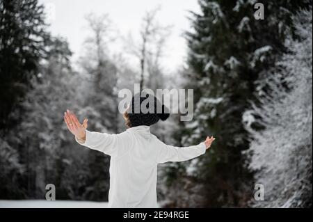 Giovane donna con cappello nero invernale in piedi in bella natura innevata con le sue braccia spalmato ampiamente. Foto Stock