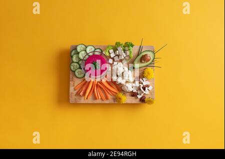 Vista dall'alto della bellissima tavola di servizio in legno piena di verdure colorate, proteine tofu e salsa di barbabietole rosa. Foto Stock