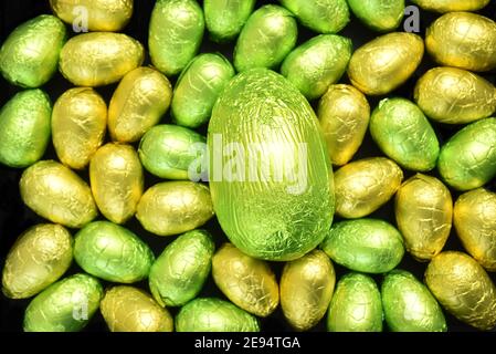 Pila o gruppo di multicolore e diverse misure di colorate uova di pasqua al cioccolato avvolte in pellicola di colore giallo e lime verde con un uovo verde grande dentro Foto Stock