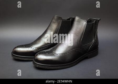 Scarpe, stivali chelsea in pelle per uomo. Moda maschile invernale, autunnale o primaverile. Calzature nere con perforazione su sfondo nero. Vendita Foto Stock