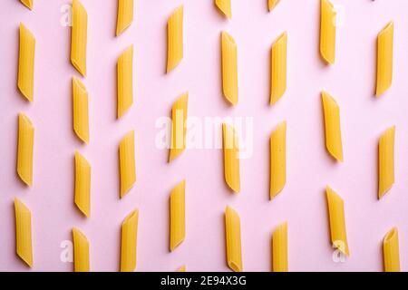 Pasta italiana, tubo crudo di penne macaroni su sfondo rosa, vista dall'alto, cibo astratto Foto Stock