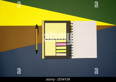 Quaderno scolastico su carta sfondo verde, giallo, marrone, grigio. Blocco note a spirale e penna di cartone artigianale Foto Stock