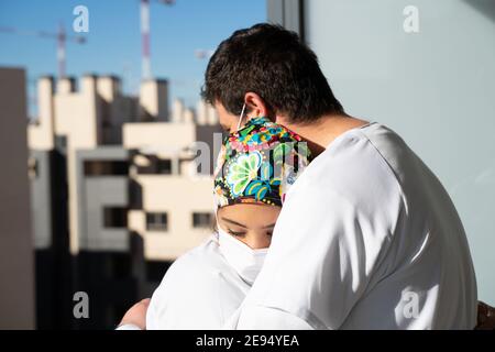 Due giovani infermieri si abbracciano e si conforgono in tempi pandemici, guardando stanchi Foto Stock