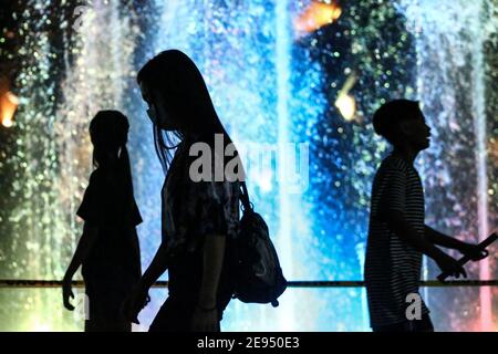 Le persone con maschere protettive camminano davanti ad una fontana al Santuario Andres Bonifacio a Manila, Filippine. Foto Stock