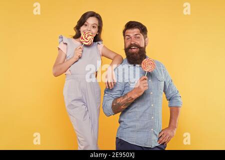 Tempo dolce. Famiglia di denti dolci sfondo giallo. Papà e figlia felici tengono le caramelle. Uomo barbuto e bambino piccolo. Dolci. Negozio di caramelle. Prodotti a base di zucchero. Le cose migliori della vita sono dolci. Foto Stock