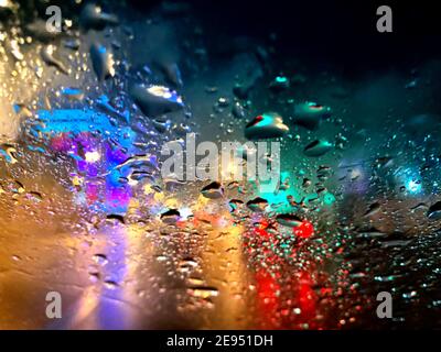Pioggia e neve bagnata sul finestrino dell'auto sullo sfondo della città e delle auto, luci multicolore della città. Foto Stock