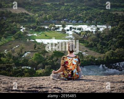 Giovane caucasica seduta e meditante sulla cima della roccia Pidurangala. Da dietro. Shot orizzontale. Sri Lanka, Asia. Foto Stock