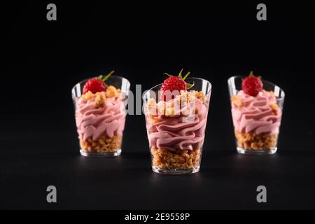 Vista in primo piano del dolce fresco fatto in casa in tre piccoli bicchieri di fila. Gustoso parfait con muesli, decorato con lamponi e whi rosa Foto Stock