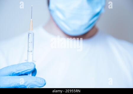 Vaccino in siringa tenuto dal medico in maschera protettiva blu e guanti in gomma Foto Stock