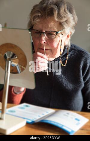 Una donna anziana esegue un test del coronavirus con tampone nasale a. casa Foto Stock