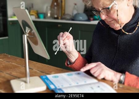 Una donna anziana controlla le istruzioni per una prova domestica controllo del tampone del coronavirus Foto Stock