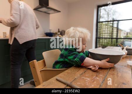 Un bambino che aiuta con la cottura in cucina che tiene una ciotola di mescolamento. Foto Stock