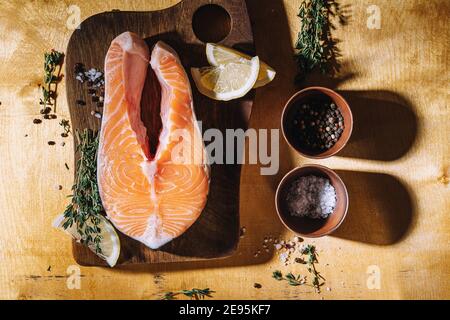 Bistecca di salmone crudo con limone e timo su tavola di legno, vista dall'alto. Illuminazione difficile Foto Stock