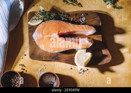 Bistecca di salmone crudo con limone e timo su tavola di legno, vista dall'alto. Illuminazione difficile Foto Stock