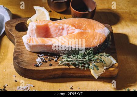 Bistecca di salmone crudo con limone e timo su tavola di legno, vista dall'alto. Illuminazione difficile Foto Stock