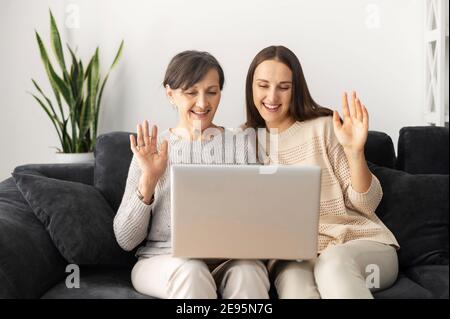 Due donne multigenerazionali usano un computer portatile per videochiamare, una madre anziana e una figlia adulta che si ondolano in una webcam seduta sul divano a casa Foto Stock