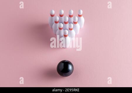 Palla da bowling e skittle bianche su sfondo rosa pastello. Concetto creativo minimo. Foto Stock