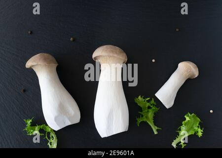 Funghi Eringi con erbe su fondo nero. Pleurotus eringi. Vegan food Concept. Flatlay. Foto Stock