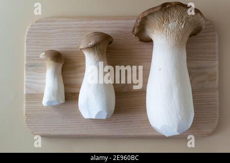 Brutto eringi funghi su un tagliere di legno su uno sfondo pastello. Pleurotus eringi. Concetto di cibo brutto. Orientamento orizzontale. Disposizione piatta. Foto Stock