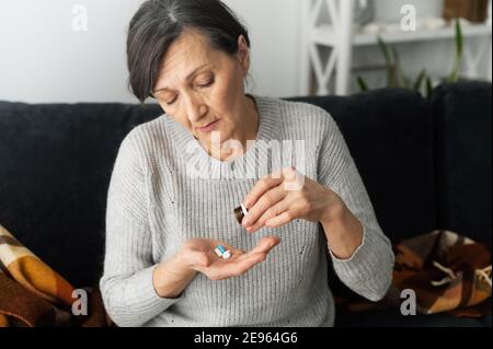 Malinconia donna anziana tiene le pillole sulla palma, triste donna matura che andrà a prendere rimedio o vitamine seduti sul divano a casa. Assistenza sanitaria e. Foto Stock