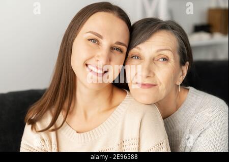 Primo piano ritratto di due donne sorridenti, una figlia cresciuta e una madre anziana guardano la macchina fotografica e sorridono, bella famiglia al coperto Foto Stock