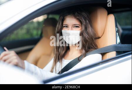 Donna guida auto mentre si indossa una maschera, coronavirus covid concetto Foto Stock