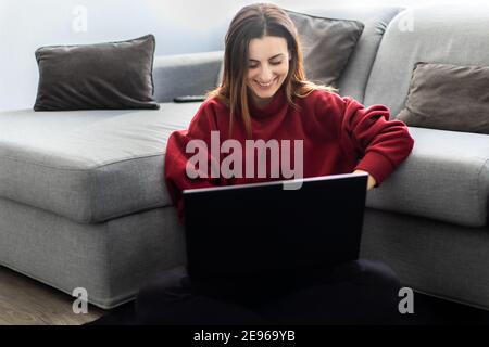 Donna che usa un computer portatile mentre si siede su un tappeto vicino un divano Foto Stock