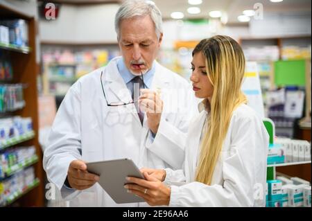 Due farmacisti parlano mentre lavorano su tablet nel loro negozio Foto Stock