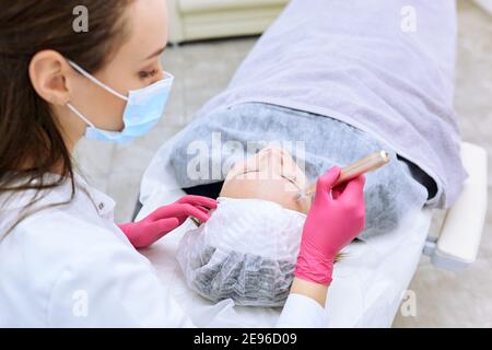 Beautician effettua iniezioni di mesoterapia, trattamenti di bellezza, cura della pelle. Donna che si cura del viso da estetista al salone termale, vista laterale. Centro benessere Foto Stock