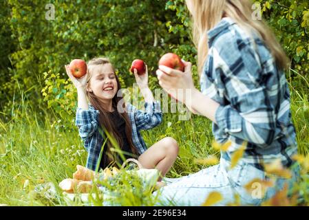 Madre con figlia nel parco. Madre che tiene le mele rosse vicino al parco eyes.Summer, cesto di frutta, pane bianco. All'aperto. Vacanze in famiglia e. Foto Stock