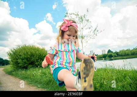 Carino bambina riccia mangiare caramelle anguria in un parco soleggiato. Bambino con lollipop all'aperto Foto Stock