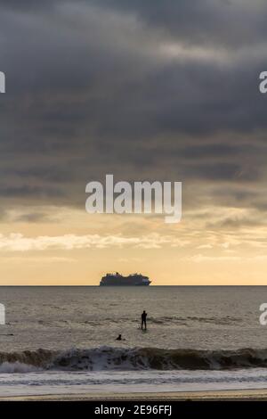 BOURNEMOUTH, INGHILTERRA - GENNAIO 17 2021: Nave da crociera ormeggiata al largo di Bournemouth a Poole Bay, ritratto, surfer paddling, copyspace in cima Foto Stock