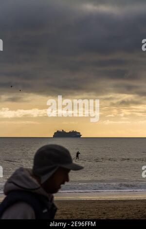 BOURNEMOUTH, INGHILTERRA - GENNAIO 17 2021: Nave da crociera ormeggiata al largo di Bournemouth a Poole Bay, Silhouette di testa del camminatore, ritratto, surfista pagaiando, copy Foto Stock