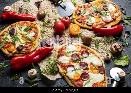 Pizze fatte in casa con funghi, salsiccia, paprika su carta di supporto vista ravvicinata Foto Stock