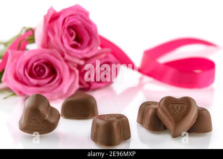 Cioccolatini a forma di cuore e bouquet di rose rosa su sfondo bianco. Concetto di San Valentino e Festa della Donna, fuoco selettivo. Foto Stock