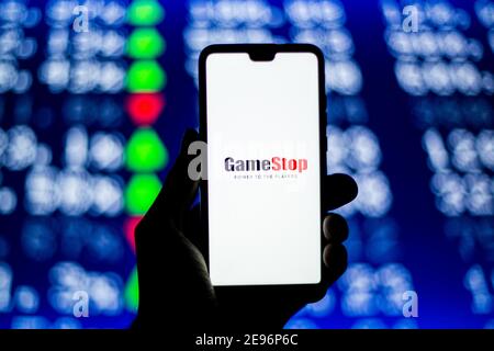 In questa illustrazione fotografica viene visualizzato un logo GameStop su uno smartphone con i numeri in maiuscolo sullo sfondo. Foto Stock
