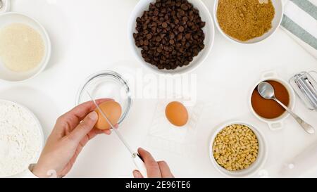 Ricetta di biscotti al cioccolato. Lo chef spezza le uova in una ciotola. Gli ingredienti per la cottura hanno bisogno di un primo piano su un tavolo da cucina bianco Foto Stock