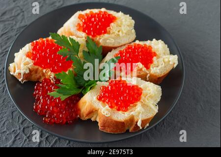 Panini con caviale rosso, limone e prezzemolo su piatto nero su fondo di cemento. Frutti di mare Foto Stock