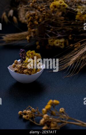 Fai da te di Pasqua. Fai da te. Decorazioni pasquali alla moda. Uova biologiche cracked con erba secca e fiori secchi su piatto. Piuma d'uccello. Spazio di copia. Biglietto d'auguri. Sfondo scuro. Foto Stock