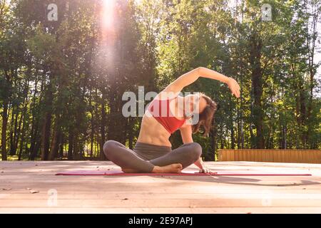 30esima donna snella con un bel corpo pratica yoga nel parco al mattino nei raggi del sole nascente. flare e abbagliare. stile di vita sano a. Foto Stock