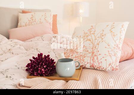 Primo piano di vassoio con fiore e grande tazza pronta per la colazione. Vassoio sul letto con cuscini grandi, freschi e puliti. Foto Stock