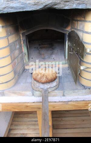 Pane fatto in casa in un forno per pizza all'aperto, la palla è stata appena tolta dal forno con la pala. Foto Stock