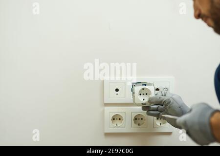 Primo piano di mani di elettricisti che indossano guanti protettivi installazione di una nuova presa in una casa Foto Stock