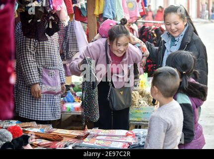 (210203) -- LIANGSHAN, 3 febbraio 2021 (Xinhua) -- Bamu Yubumu (C) seleziona nuovi vestiti per i suoi bambini in un mercato di strada nel villaggio di Taoyuan, nella contea di Yuexi, nella prefettura autonoma di Liangshan Yi, nella provincia sudoccidentale del Sichuan, 22 gennaio 2021. Una giovane madre si è arduamente appoggiata in avanti per bilanciare il peso di un bagaglio oversize sulla schiena e di un piccolo bambino nel braccio, mentre ha combattuto i suoi passi avanti. Questa era l'immagine che il reporter di Xinhua Zhou KE catturò vicino alla stazione ferroviaria di Nanchang, nella provincia di Jiangxi, nella Cina orientale, il 30 gennaio 2010. La foto dal titolo 'il bambino, la mamma ti porta a casa' tou Foto Stock